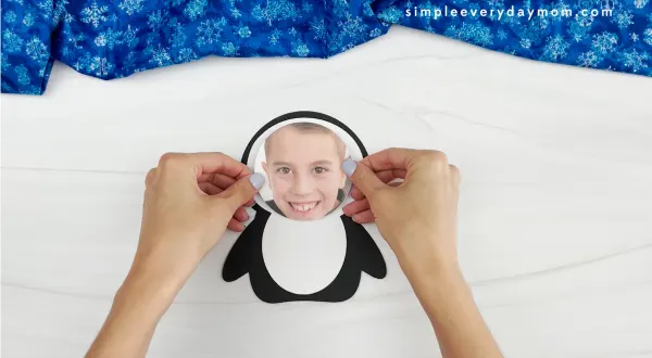 hands placing picture of child onto head of photo penguin craft