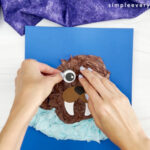 hand placing eyes onto head of walrus tissue paper craft