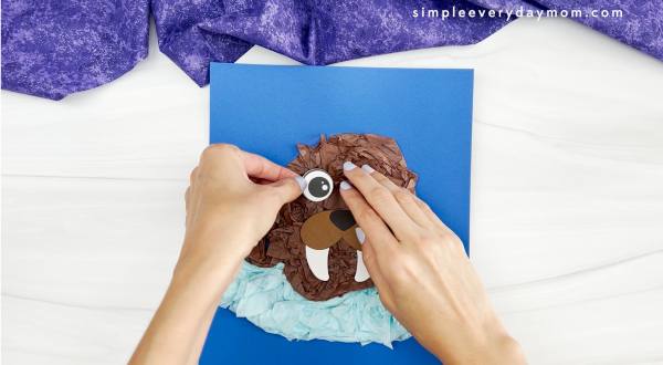 hand placing eyes onto head of walrus tissue paper craft