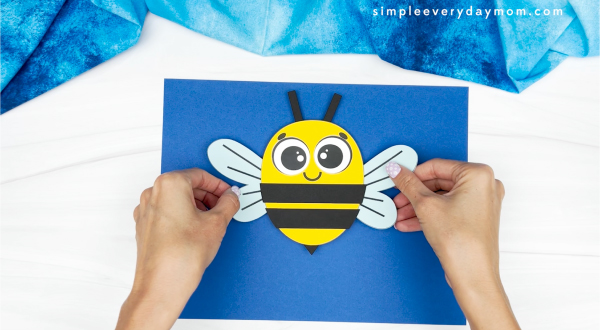 hands gluing finished bee onto backdrop paper