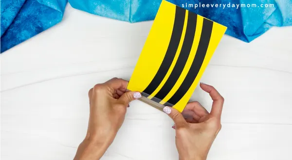 hands gluing striped black and yellow body onto tp roll