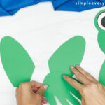 hands gluing paper hands onto frog legs