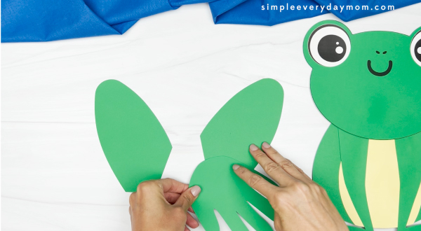 hands gluing paper hands onto frog legs