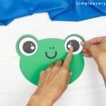 hands gluing eyes onto frog head