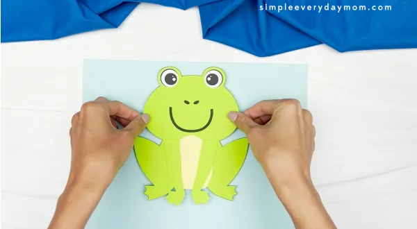 hands gluing finished frog onto sheet of paper