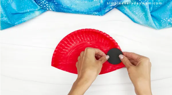 hands gluing black dots onto paper plate