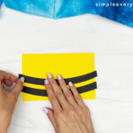 hands gluing black stripes onto bee body