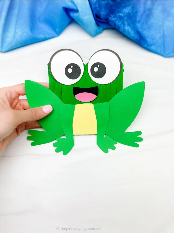 hand holding single example of finished popsicle stick frog craft