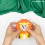 hands gluing lion face to paper cup
