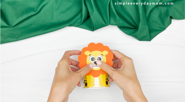hands gluing lion face to paper cup