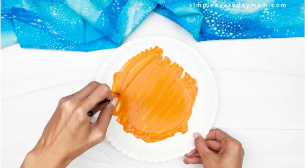 hands painting paper plate orange