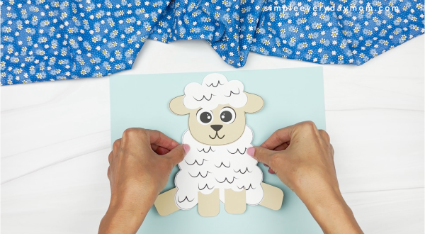 hands gluing sheep onto backdrop piece of paper