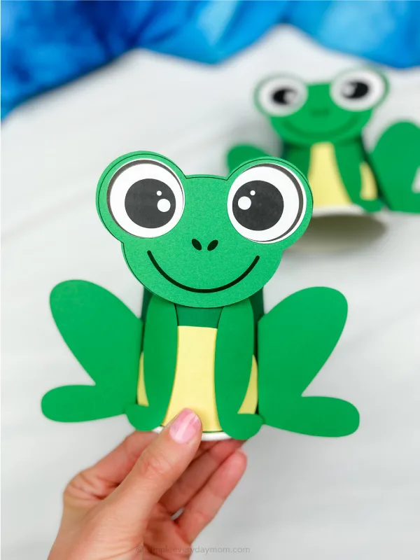 hand holding finished example of frog paper cup craft with another in background