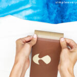 hands gluing monkey body to toilet paper roll