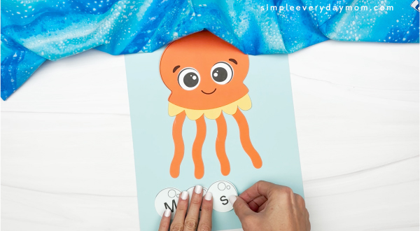 hands gluing letters to name onto sheet of paper below jellyfish