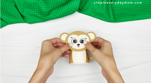 hands gluing monkey face to paper cup