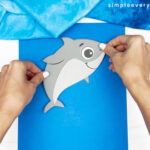 hands gluing shark to blue backdrop