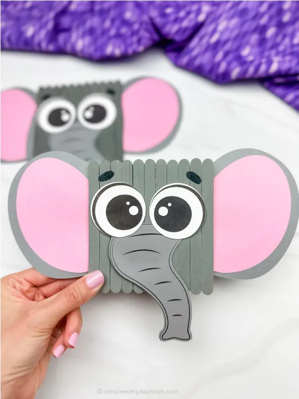 hand holding popsicle stick elephant craft with another in the background