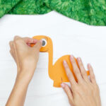 hands gluing eye to dinosaur