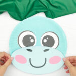 hand gluing the mouth and the face of dinosaur paper plate craft