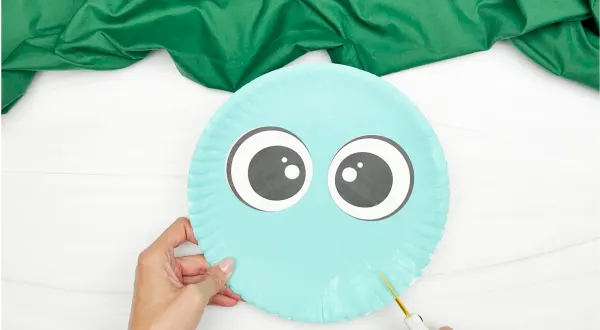 spreading glue at the bottom of the eyes of dinosaur paper plate craft