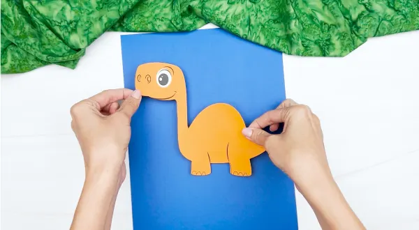 hands gluing dinosaur to background sheet of paper