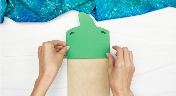 hands gluing piece of dinosaur to paper bag