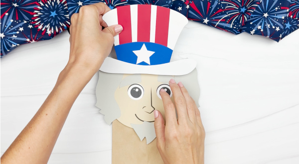hands gluing hat to Uncle Sam puppet craft