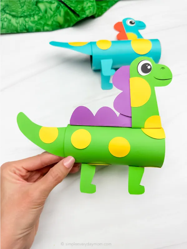 hand holding green dinosaur tp craft with another example in background