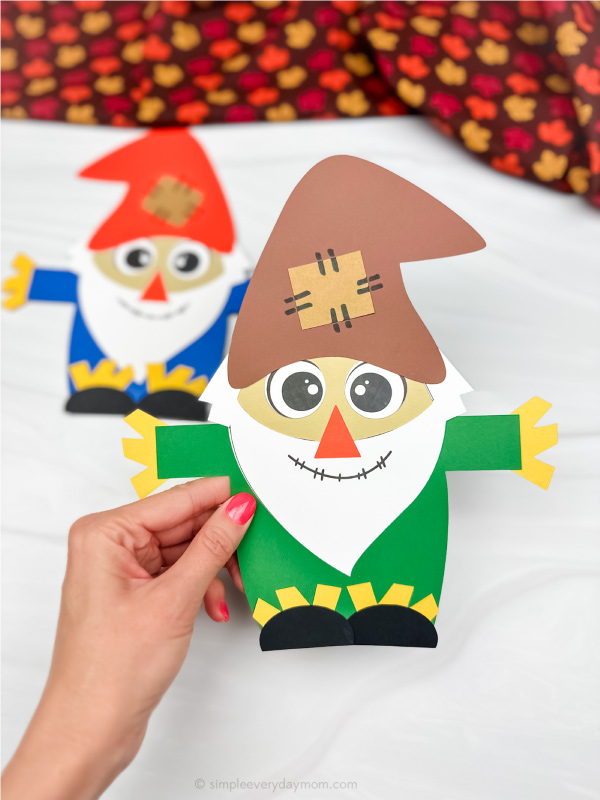hand holding green dressed scarecrow with another gnome in background