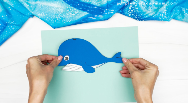 hands gluing whale to background paper