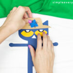 hands gluing hat to Pete the cat scarecrow craft