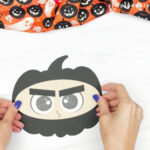 hands gluing ninja face to pumpkin