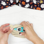 hands placing bandage ends onto head of mummy card craft