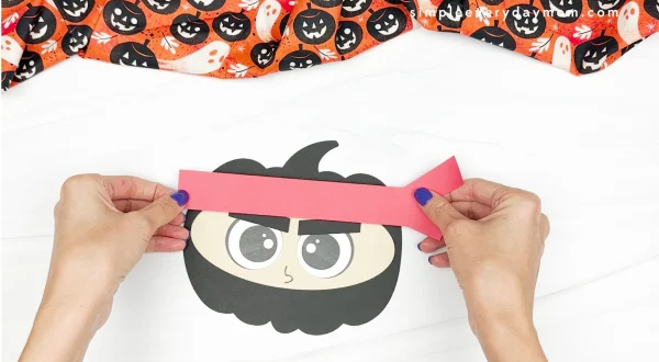 hands gluing ninja headband to pumpkin