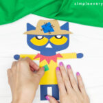 hands gluing shirt pieces to Pete the cat scarecrow craft