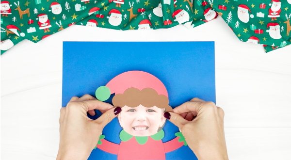 hand gluing the photo elf to the construction paper background