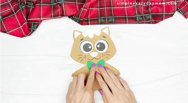 hands gluing bowtie to Gingerbread cat craft body