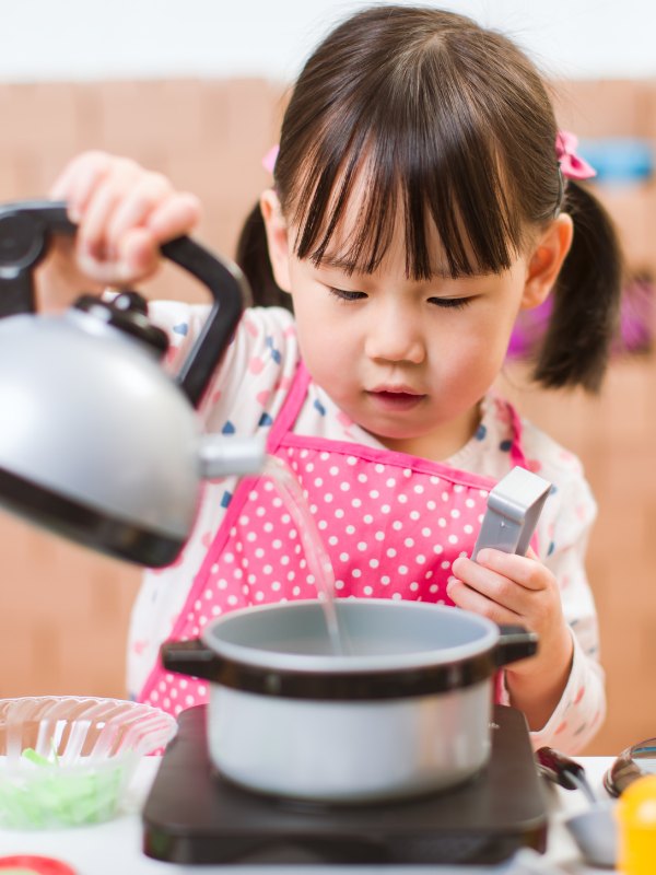little girl pouring water out of pretend play tea kettle into pot