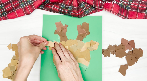 hand gluing the upper part of the face of torn paper reindeer craft