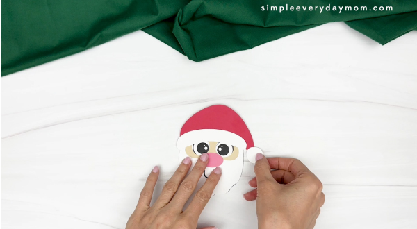 hand gluing the pom to the tip of the hat of santa paper cup craft