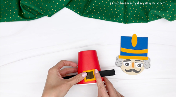 hand gluing the belt of the nutcracker paper cup craft