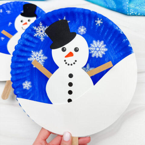 hand holding the snowman paper plate craft with background on side