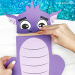 hand gluing the head to the body of dragon puppet craft