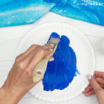 painting blue paint on paper plate