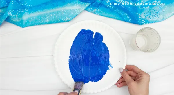 painting blue color on paper plate of snowman craft