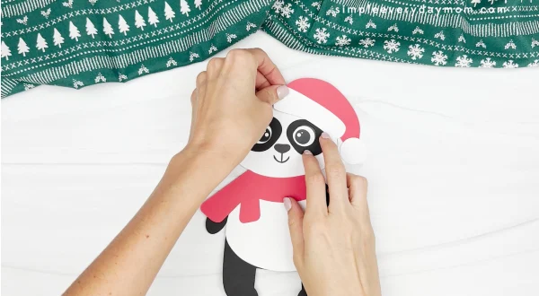 hand gluing the hat to the head of panda christmas craft