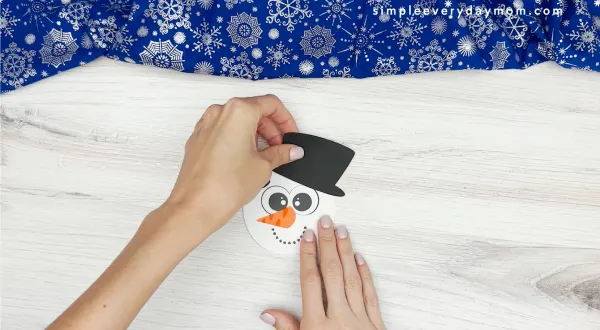 hand gluing the hat to the snowmans head