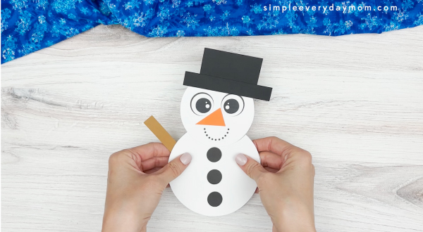 hand gluing the stick arms of the snowman shape craft