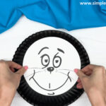 hand gluing the face to the paper plate